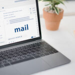 Open laptop on a desk displaying an email inbox, with folders and messages visible on the screen.