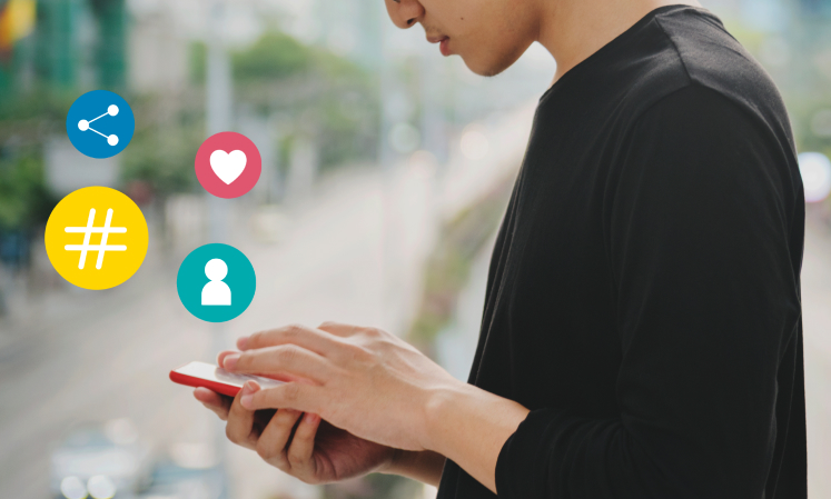 Person using a smartphone with social media icons - share, heart, hashtag, and profile, floating beside them.